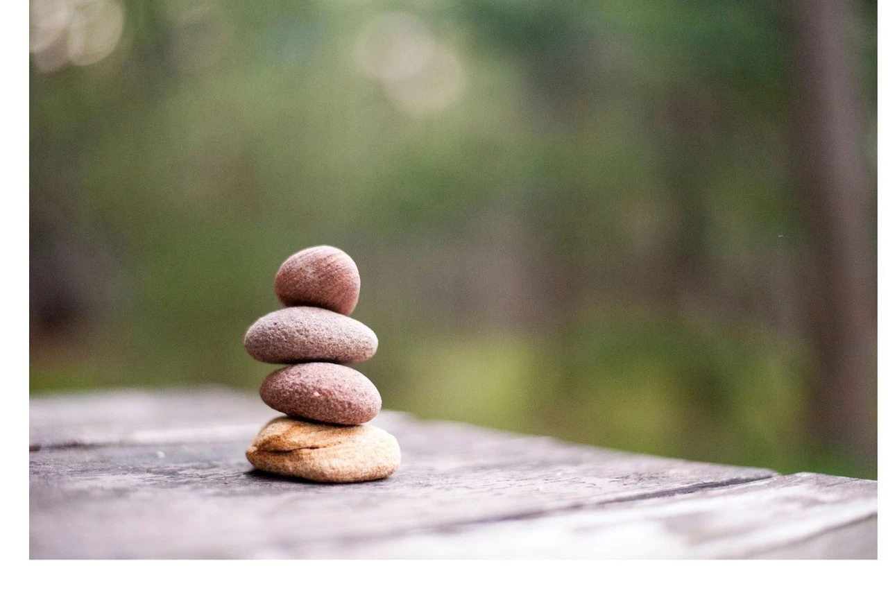 4 galets empilés sur une table dans la nature représentant symboliquement l'idée d'équilibre, de calme, et de simplicité, des valeurs qui s'harmonisent avec la sophrologie et la gestion du stress au travail. Les galets empilés évoquent la notion de stabili