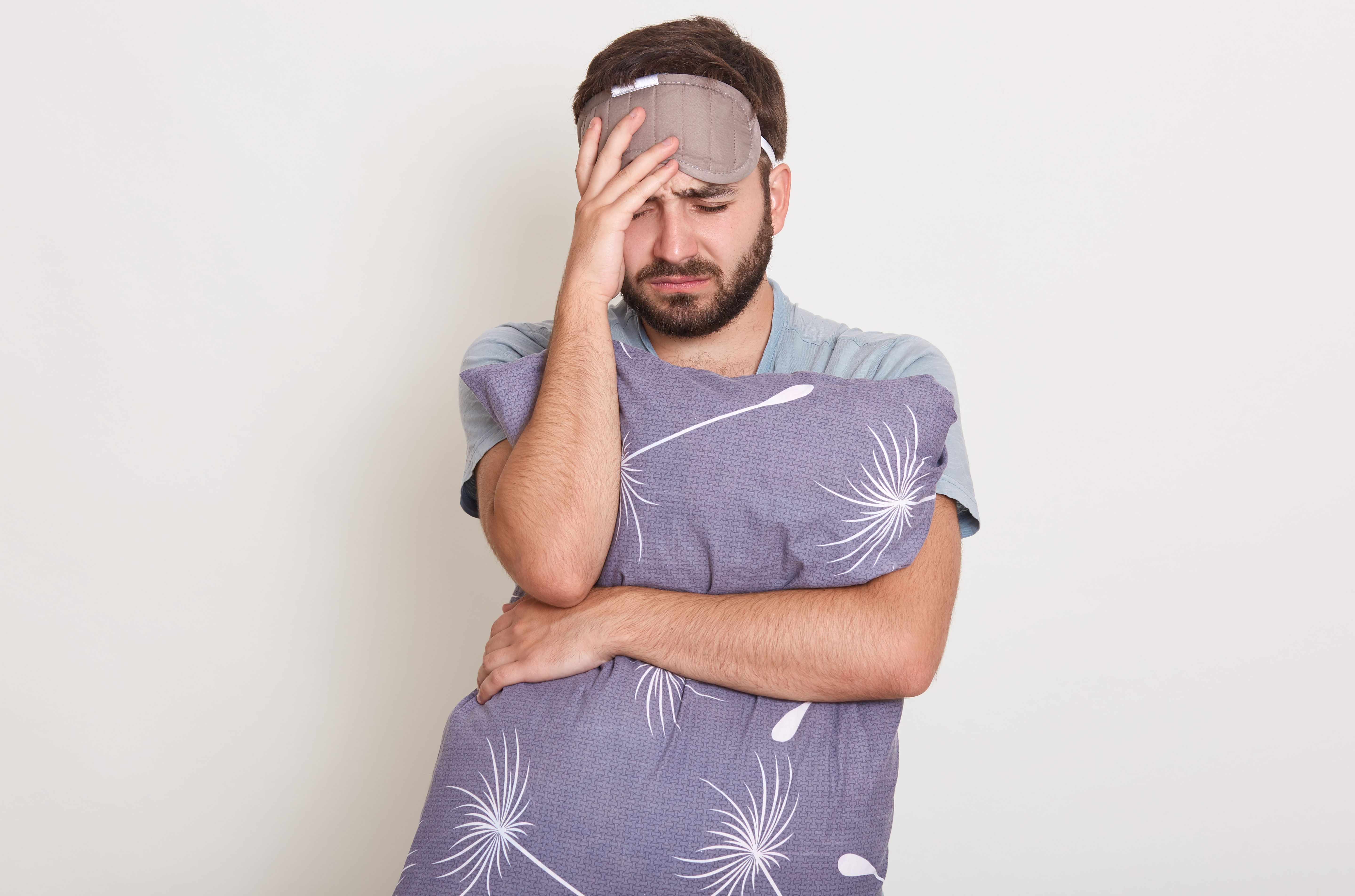 homme avec un oreiller dans les bras et masque de nuit n'arrivant pas à dormir