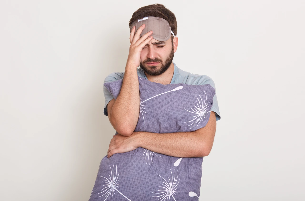homme avec un oreiller dans les bras et masque de nuit n'arrivant pas à dormir