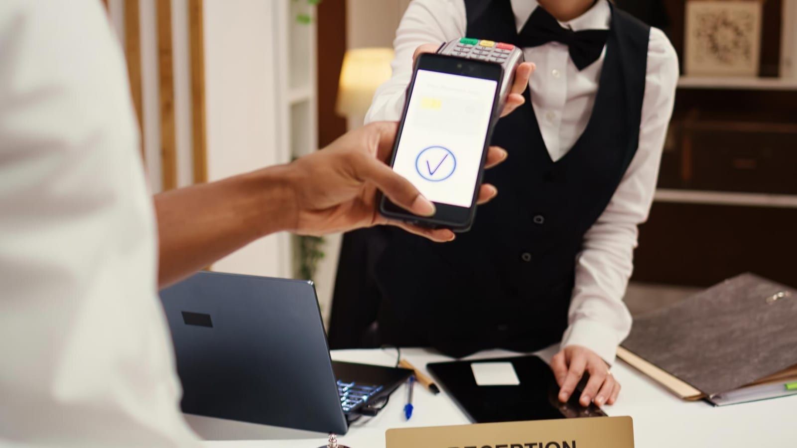 Terminal płatniczy i smartfon na drewnianej ladzie recepcyjnej w butikowym hotelu