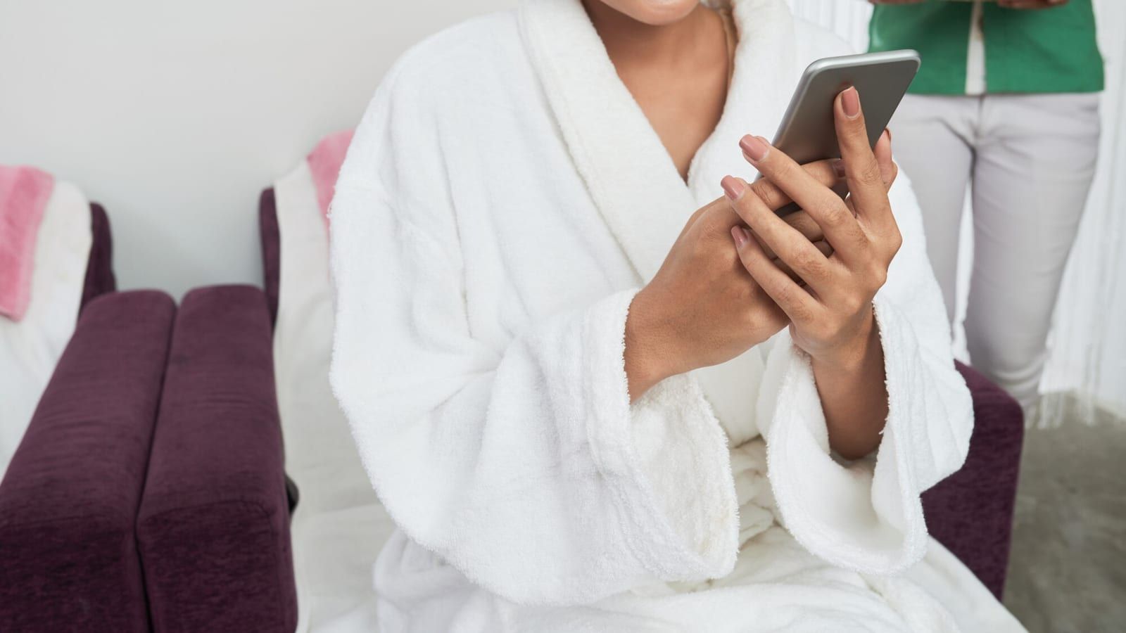 Gość hotelowy rezerwujący masaż na smartfonie, leżąc na leżaku przy basenie