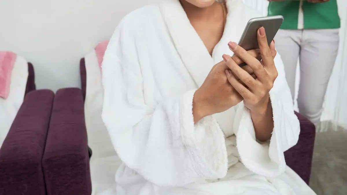 Gość hotelowy rezerwujący masaż na smartfonie, leżąc na leżaku przy basenie