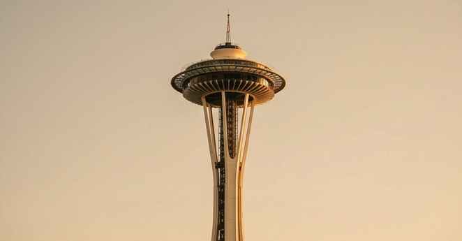 Editorial travel photo of Seattle Space Needle shot from below against a clear sky, warm golden afternoon light, earthy tones of taupe and gold, slightly desaturated modern editorial travel photography style, no cars visible in frame