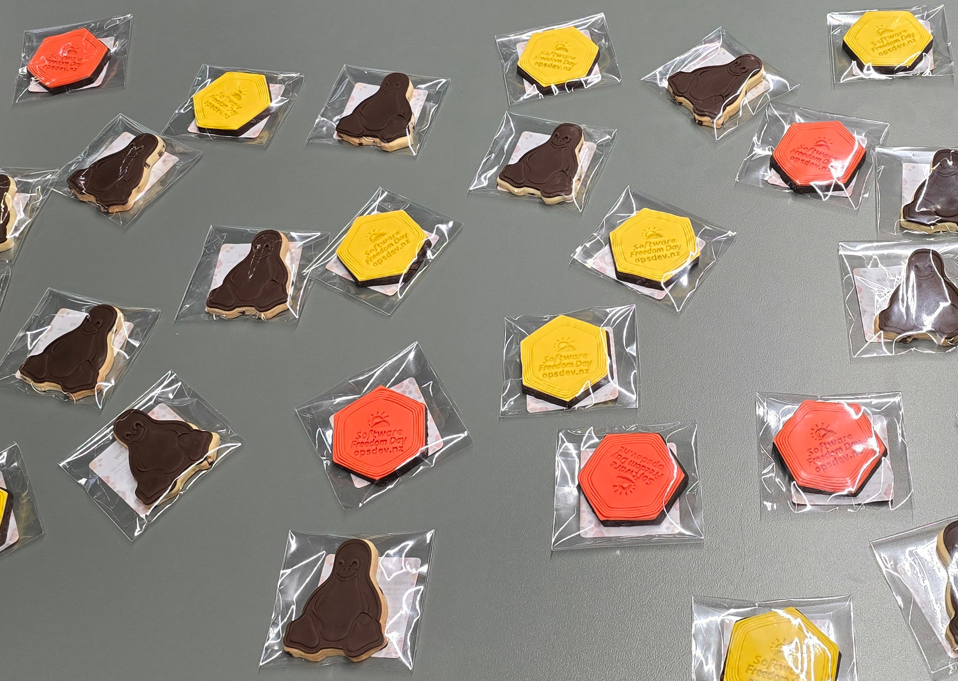 Tux-shaped chocolate chip cookies with chocolate icing, and orange and yellow hexagon-shaped Software Freedom Day cookies